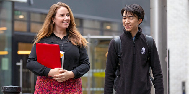 Two students walk happily with university in background
