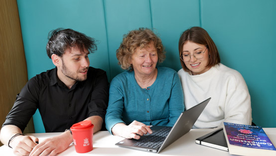 Three individuals look at laptop screen in academic setting