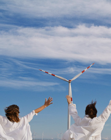 Two people raising arms towards wind turbine under blue sky