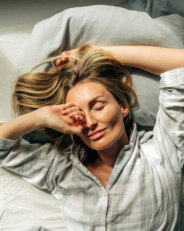 Person lies In bed after waking up and stretches and rubs eyes