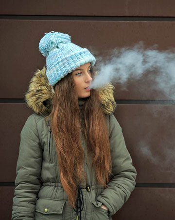 Teenager smoking an electronic cigarette on the street in the winter