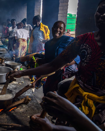People preparing food at a row of large cooking stoves in The Kitchen in Malawi.