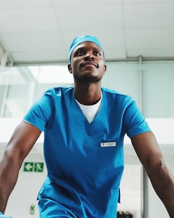 Healthcare students or professionals in blue scrubs participate in a clinical training activity, viewed from a low-angle perspective in a healthcare setting.