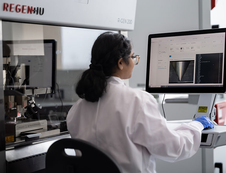 Researcher operating advanced laboratory equipment while reviewing scientific data displayed on a computer monitor in a biomedical research laboratory.