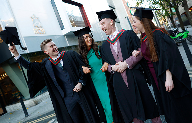 Four RCSI BSc Physiotherapy graduates wearing black graduation gowns walk along York Street.