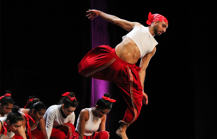 A dancer, dressed in red trousers and a white top jumps in the air.