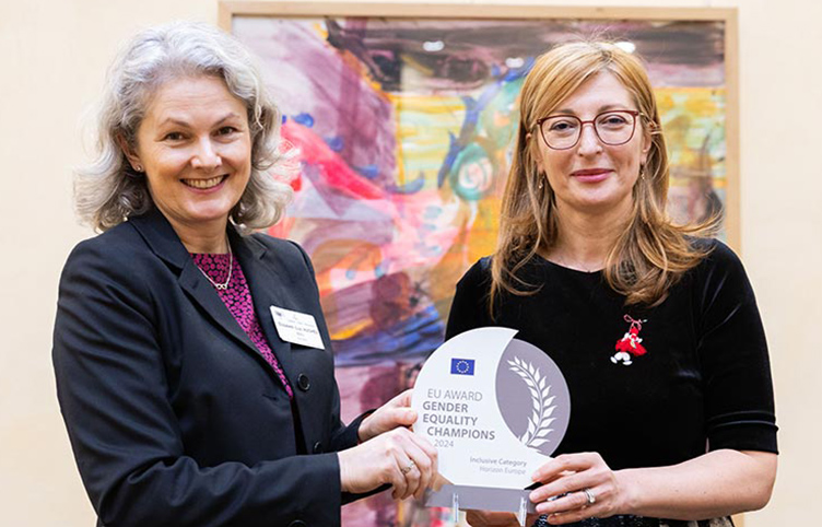 Two people hold an award and smile at the camera.