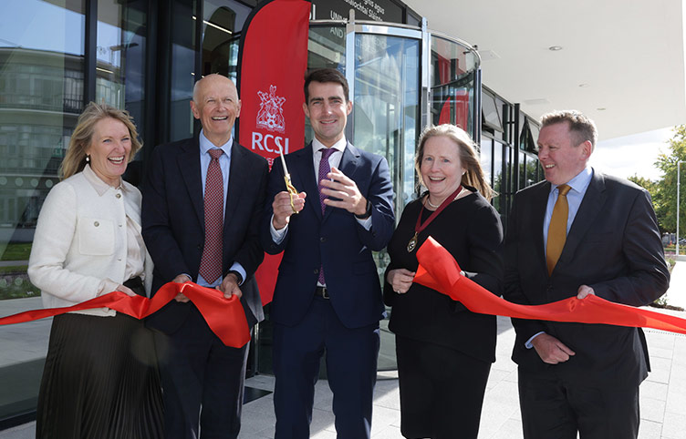 Minister for Finance, Jack Chambers TD uts the ribbon on a new RCSI building as four other people smile and look on. 