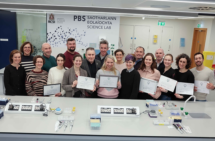 A large group of people are pictured in an RCSI lab holding up certificates.
