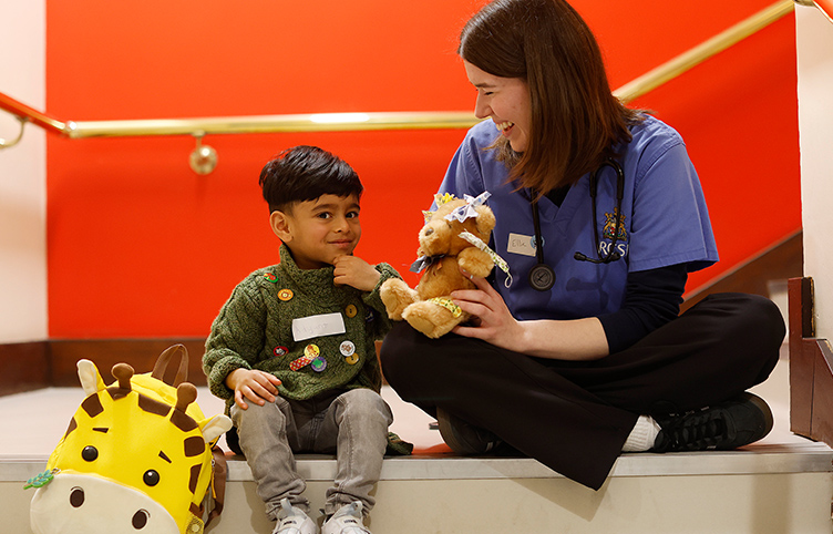 An RCSI Medicine student sits with a young boy and his teddy bears on a stairs