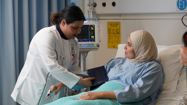 A nurse taking the vital signs of a woman in a hospital bed.