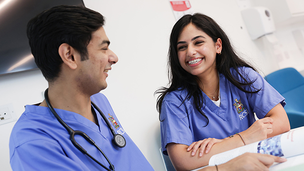 Two RCSI Medicine students wearing scrubs smile at each other