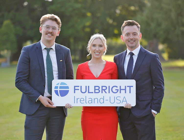 Three individuals stand with Fulbright Ireland-USA placard in a park