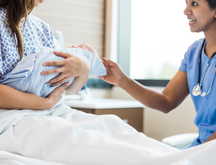 A woman on a hospital bed holding her newborn baby, with a nurse at the side of the bed.