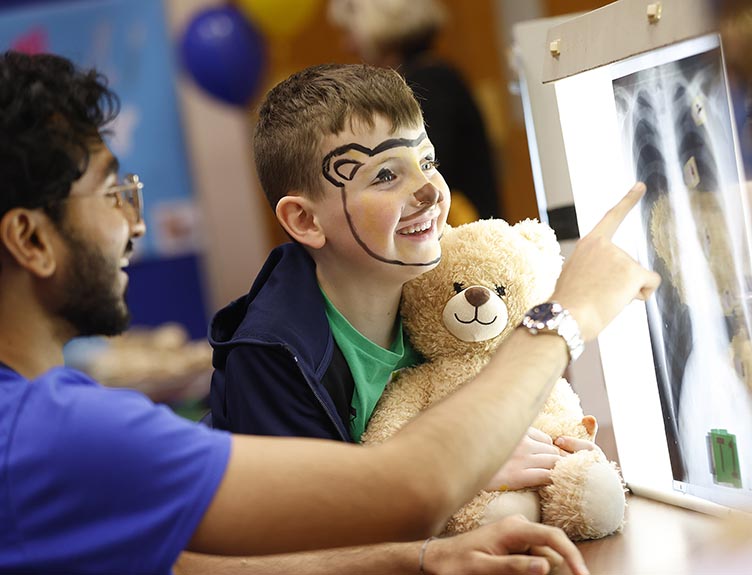 A clinician, a young boy and a teddy bear examine an X-ray image.