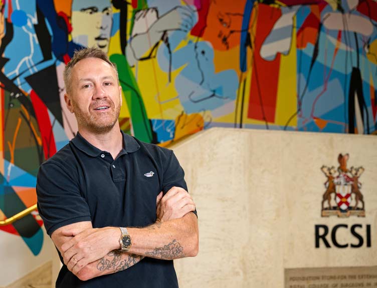 Alumni Awards mural Artist stands in front of large scale colourful artwork on university wall