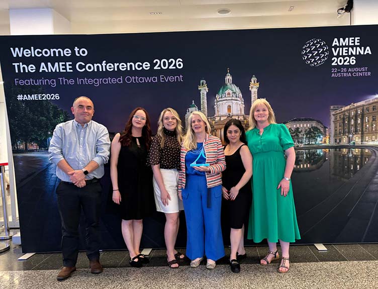 RCSI SIM group standing in front of a large AMEE Conference 2026 event backdrop featuring Vienna landmarks, with one attendee holding an award.