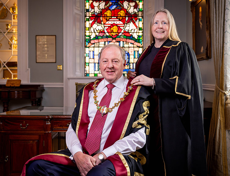 Professor Michael Kerin – in official robes and seated in front – receives the official chain of office from outgoing RCSI President Professor Deborah McNamara, who stands behind, also in official robes. 