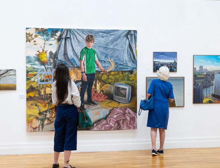 Two people look at artworks at exhibition