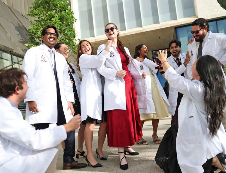 Students in RCSI gather outdoors during the White Coat Ceremony for a group photo while a person in the foreground takes a picture with a camera.