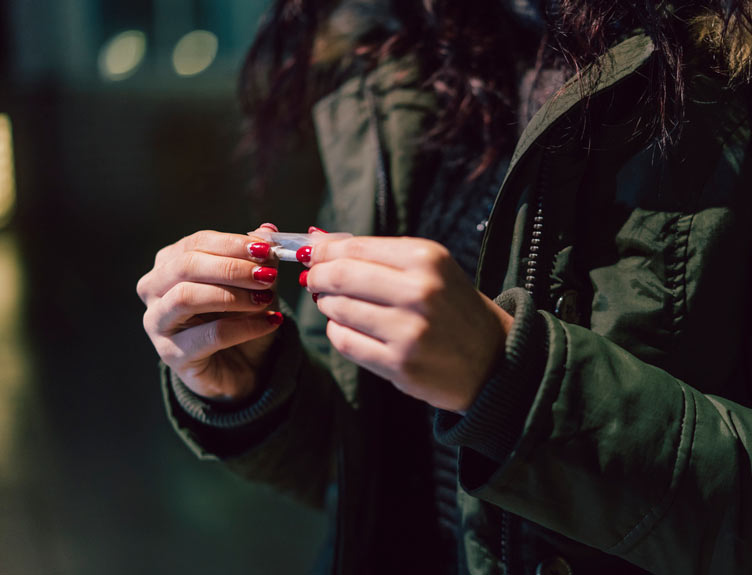 Young adult rolling a cigarette outdoor in the city at night.