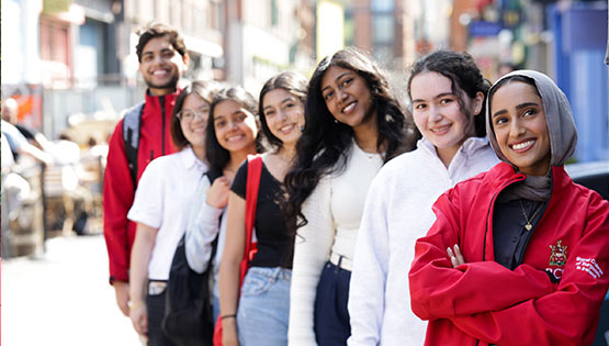 Group of seven students standing together in a line on a city street, some wear RCSI branded clothing. 
