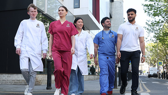 Group of RCSI healthcare students walking together outside the RCSI campus building, wearing clinical uniforms and white coats.