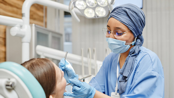 Portrait of young dentist working with patient sitting in dental chair at clinic