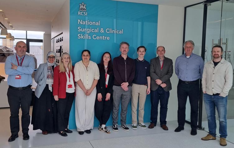 Group photo of 10 people standing in a bright indoor foyer beneath at RCSI's National Surgical and Clinical Skills Centre.