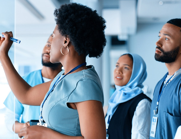 A diverse group of medical professionals collaborate while one uses a whiteboard to write down points. 