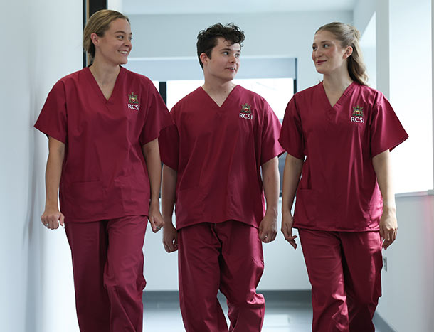 Three Dentistry students in RCSI clinical uniforms walking together through a university corridor.