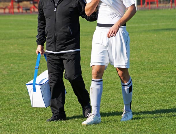 A medic helps a player walk off the pitch for treatment at a soccer match.