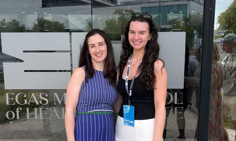 Dr Muirne Spooner and Katie Howe pose together in front of glass building