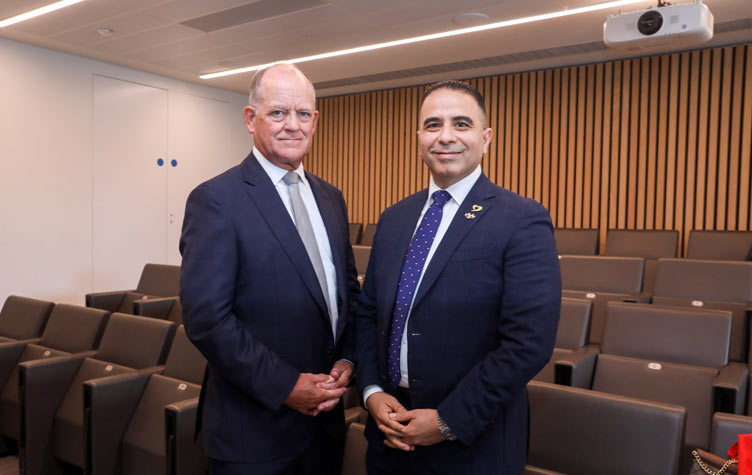 Mr David Moore and Dr Ahmed Eissa in business attire stand in a modern auditorium with tiered seating and a wood-panelled wall in the background.