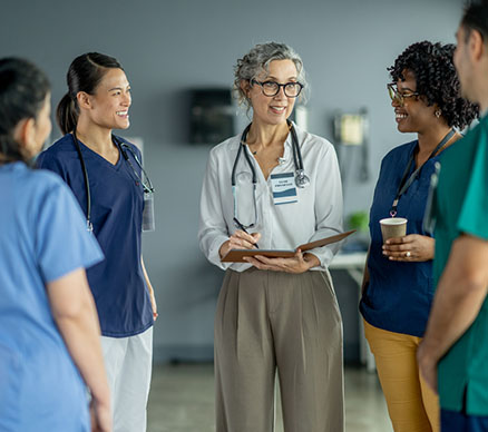 A surgical team of five conferring, led by a doctor with a clipboard.