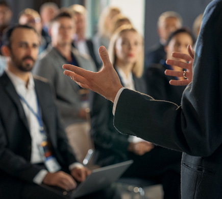 A person standing and making a presentation in front of a seated audience.