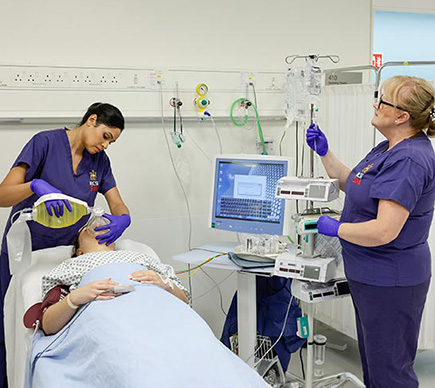 Two nurses with IV, oxygen mask and monitoring equipment care for a patient who is in an ICU bed.