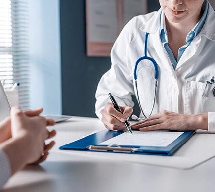 A doctor taking case notes with a patient at a desk.