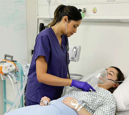 A nurse cares for a patient who is in bed and wearing a breathing mask.