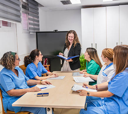 A group of nurses sit at a table while a manager is standing and making a presentation.