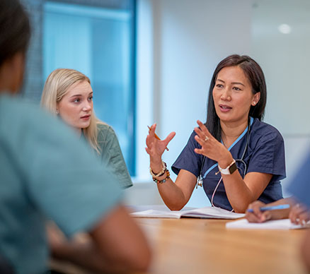 A nurse explaining a point among clinical colleagues at a conference table.