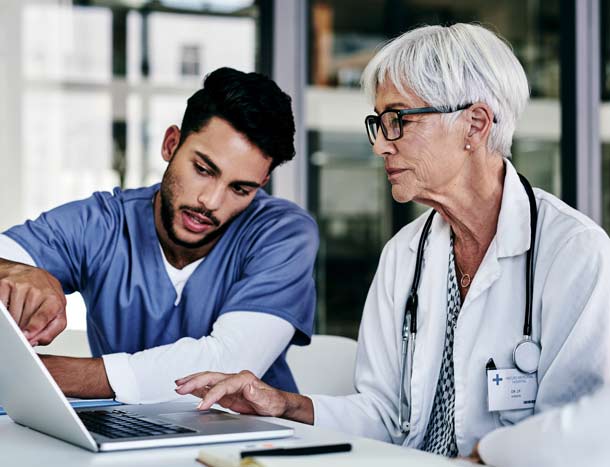 Two healthcare professionals collaborating at a desk, reviewing information on a laptop while discussing a document.