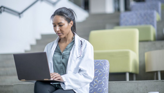 A professional in a white coat works on a laptop