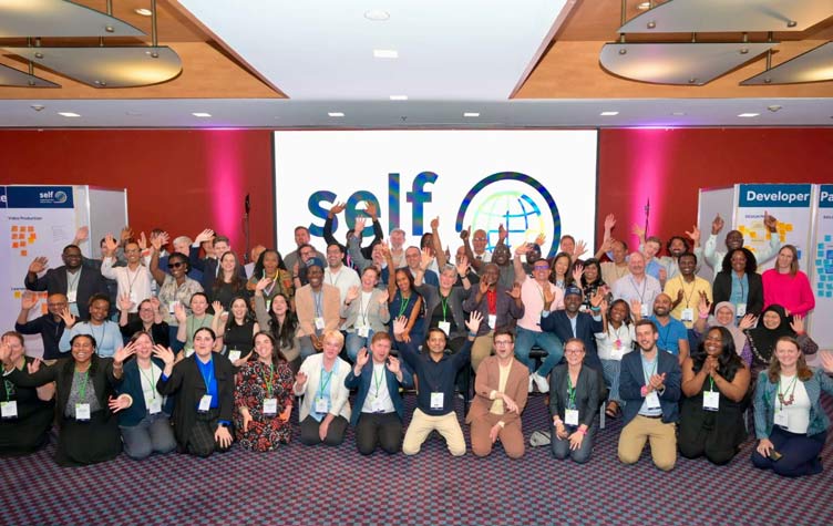 Large group wave to camera in front of screen